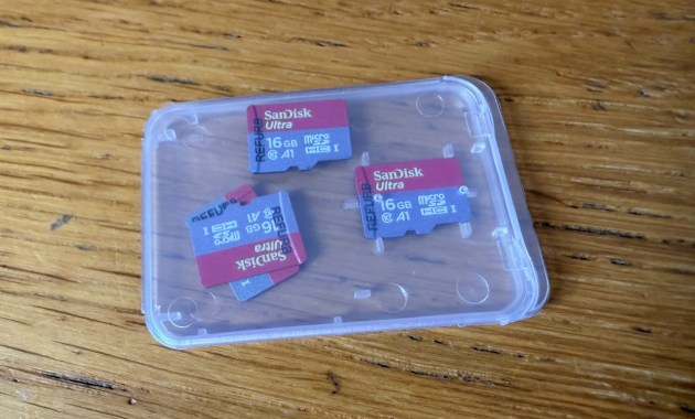 Three SanDisk Ultra 16GB microSD cards labelled refurbished in a plastic case on a wooden table